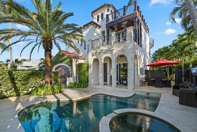 back of house with a balcony, a patio, and a pool with hot tub