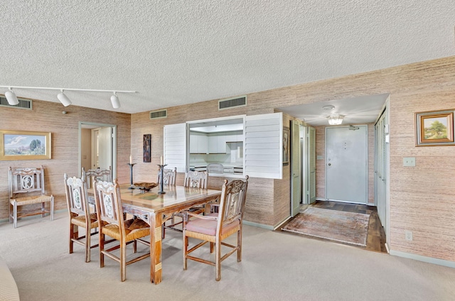 dining area with light colored carpet, a textured ceiling, and rail lighting