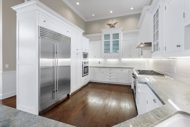 kitchen with ornamental molding, backsplash, dark wood-type flooring, white cabinetry, and built in appliances