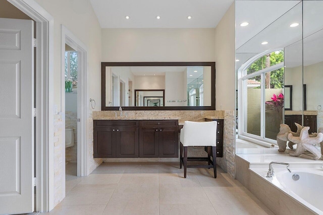 bathroom with tile patterned flooring, tiled tub, vanity, and toilet