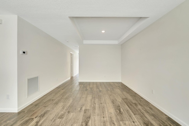 unfurnished room featuring a textured ceiling, a tray ceiling, and light hardwood / wood-style floors