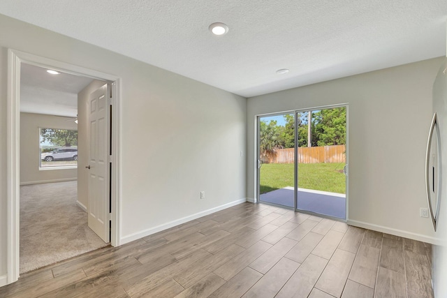 unfurnished room featuring a textured ceiling, light hardwood / wood-style flooring, and plenty of natural light