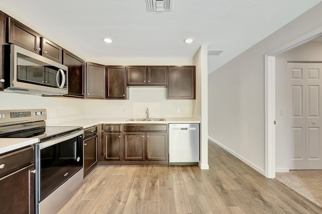 kitchen featuring dark brown cabinetry, sink, a textured ceiling, light hardwood / wood-style flooring, and appliances with stainless steel finishes