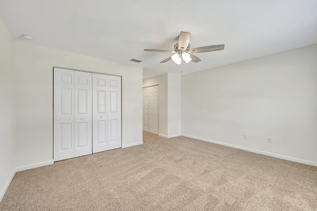 unfurnished bedroom with light carpet, multiple closets, and ceiling fan