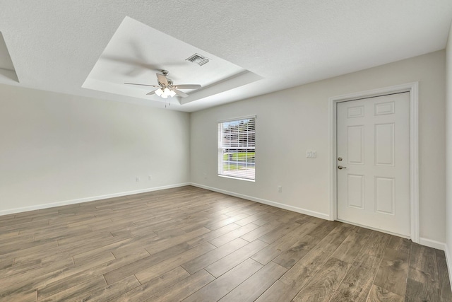 unfurnished room with ceiling fan, a textured ceiling, a raised ceiling, and light hardwood / wood-style floors