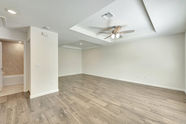 empty room with light wood-type flooring, a textured ceiling, a tray ceiling, and ceiling fan