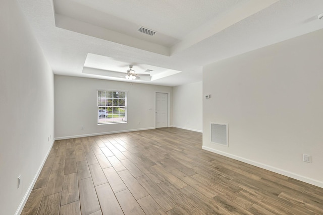 empty room with a textured ceiling, a tray ceiling, ceiling fan, and hardwood / wood-style flooring