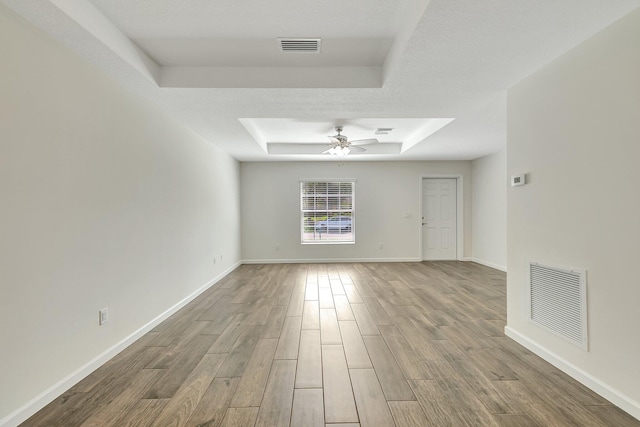 spare room with ceiling fan, a textured ceiling, light wood-type flooring, and a raised ceiling