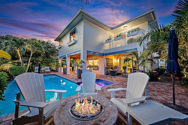 pool at dusk with a patio area, a diving board, and a fire pit