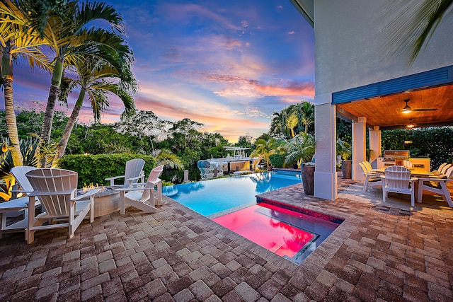 pool at dusk featuring an in ground hot tub and a patio