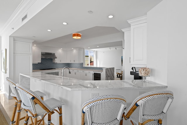 kitchen with white cabinets, light stone countertops, kitchen peninsula, and exhaust hood