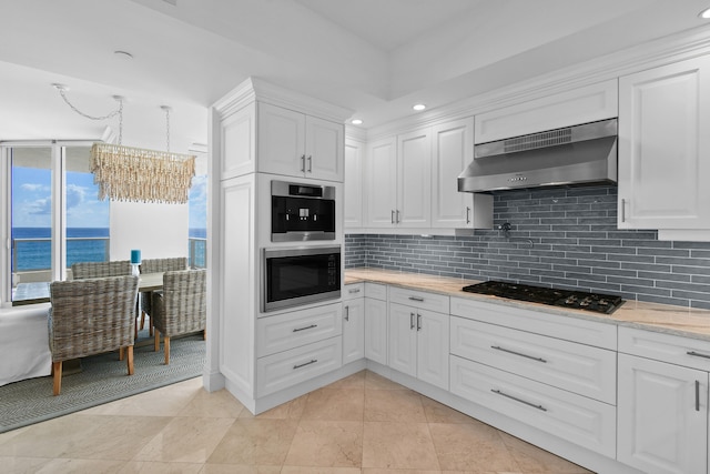 kitchen with black gas cooktop, wall chimney exhaust hood, white cabinetry, a notable chandelier, and a water view