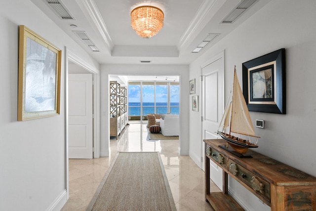 hallway featuring a raised ceiling, crown molding, a chandelier, and a water view