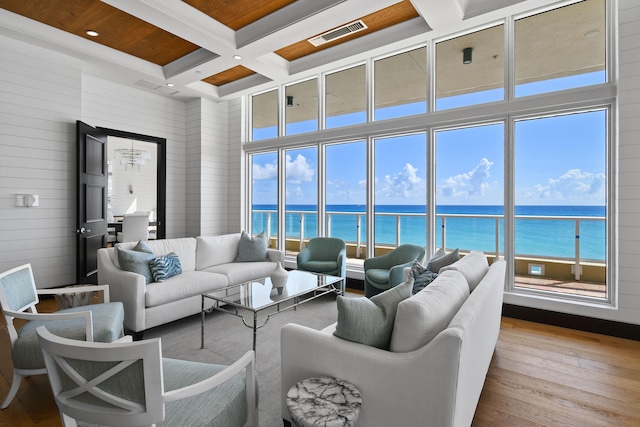 living room with light wood-type flooring, a water view, coffered ceiling, and beamed ceiling