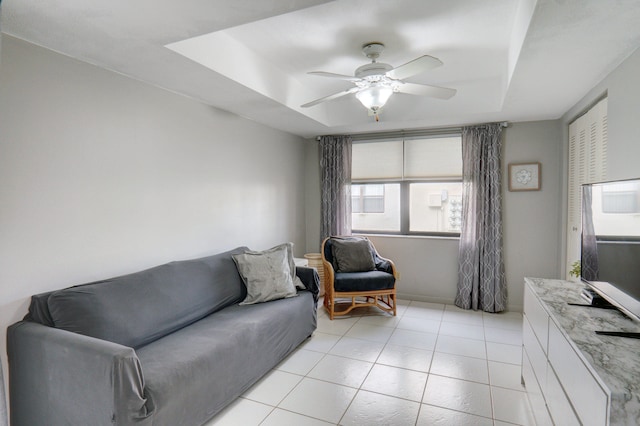 living room featuring a raised ceiling, ceiling fan, and light tile patterned floors