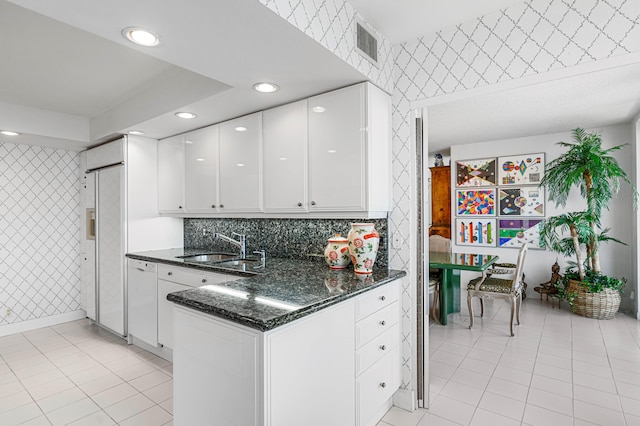 kitchen featuring white cabinets, light tile patterned floors, sink, dark stone counters, and decorative backsplash