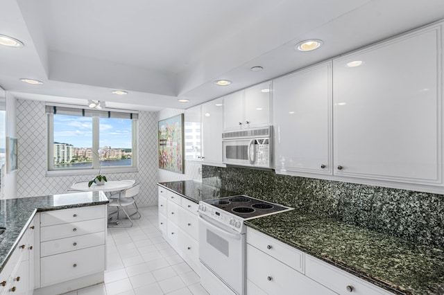 kitchen with light tile patterned flooring, tasteful backsplash, white appliances, white cabinetry, and dark stone counters