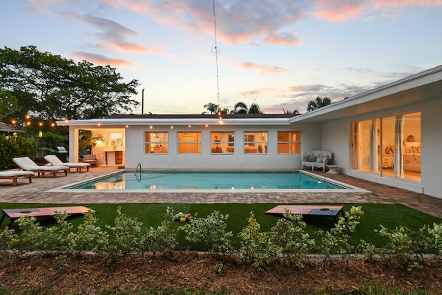 8045 W Lake Dr, Lake Clarke Shores, FL 33406 - back of house at dusk with a patio area, an outdoor pool, a lawn, and stucco siding