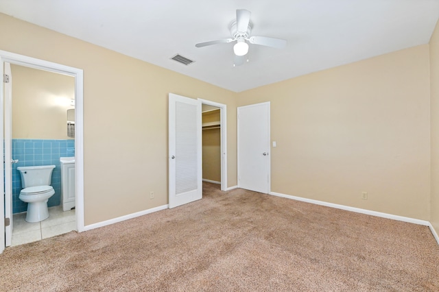 unfurnished bedroom featuring ensuite bath, ceiling fan, tile walls, light colored carpet, and a closet