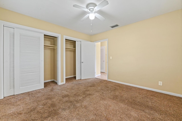 unfurnished bedroom with ceiling fan, light carpet, and two closets