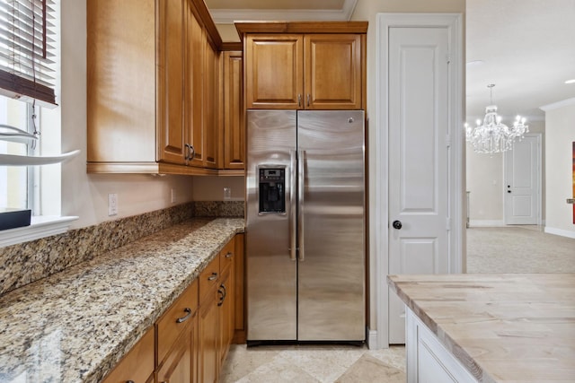 kitchen featuring light stone counters, hanging light fixtures, stainless steel fridge, a notable chandelier, and crown molding