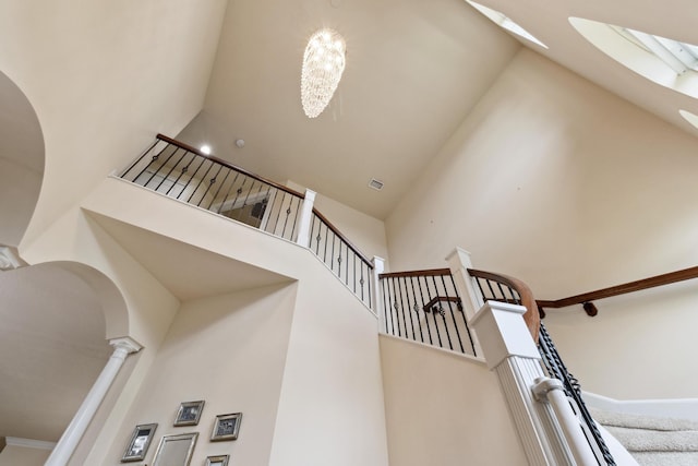 staircase with decorative columns, a towering ceiling, and a notable chandelier