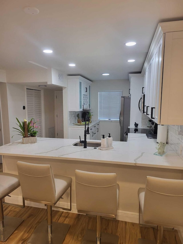 kitchen with stainless steel appliances, white cabinetry, kitchen peninsula, tasteful backsplash, and dark hardwood / wood-style floors