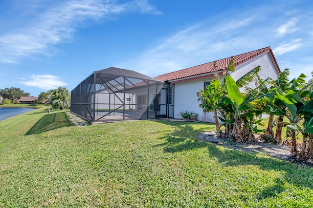 rear view of property with a tiled roof, glass enclosure, stucco siding, a patio, and a lawn