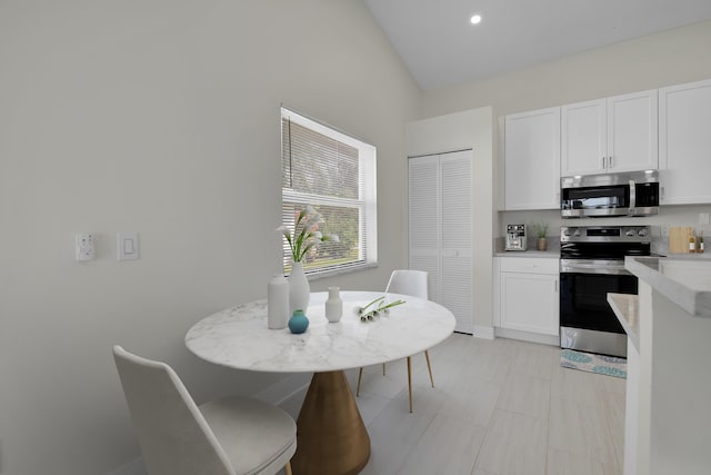 kitchen with white cabinets, stainless steel appliances, baseboards, lofted ceiling, and light countertops