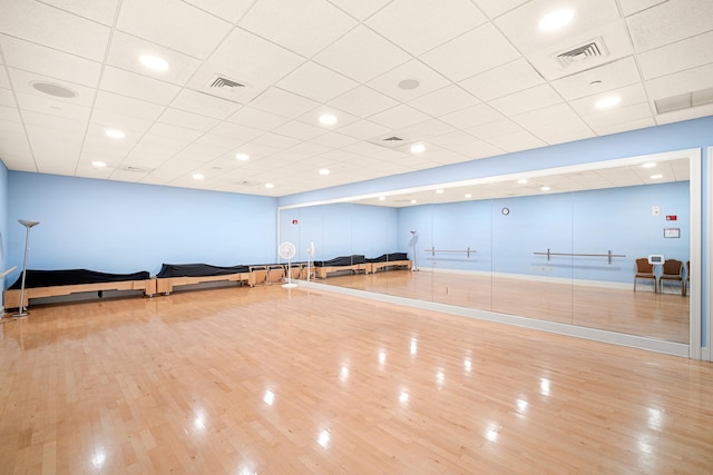 exercise area featuring light wood-type flooring and a drop ceiling