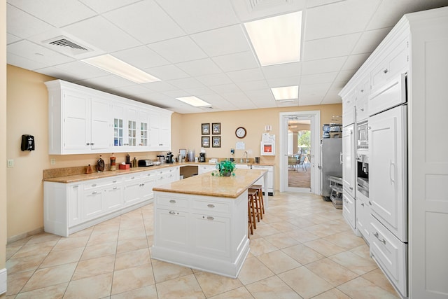 kitchen with white cabinets, a kitchen island, dishwasher, a breakfast bar area, and light tile patterned floors