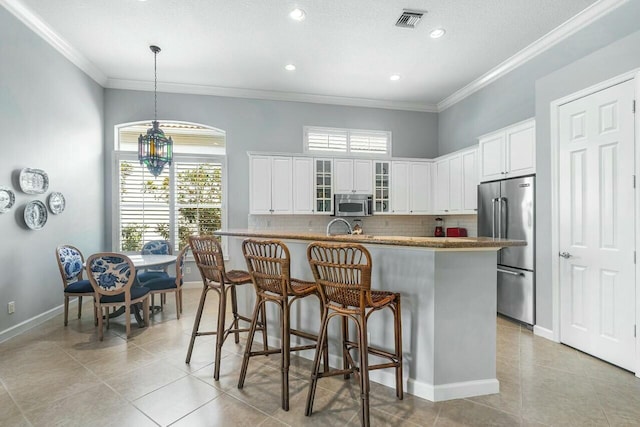 kitchen with stainless steel appliances, white cabinets, hanging light fixtures, ornamental molding, and tasteful backsplash