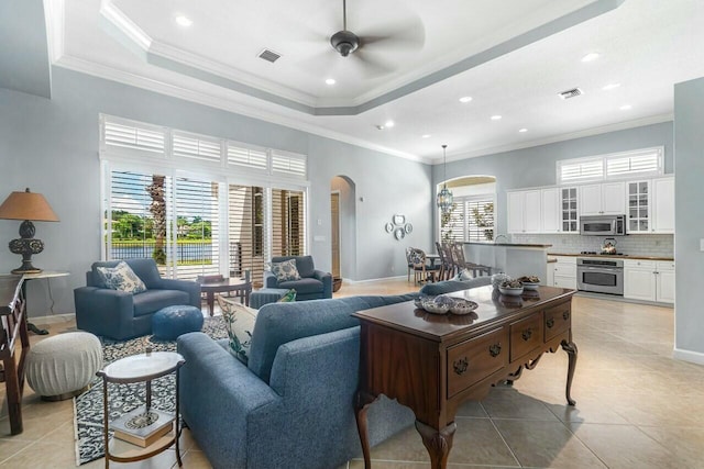 living room featuring a tray ceiling, ornamental molding, and light tile patterned flooring