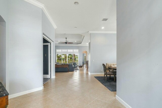 corridor featuring a tray ceiling, light tile patterned floors, and crown molding