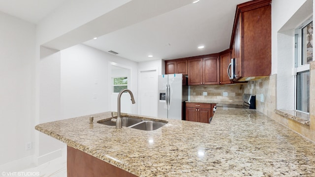 kitchen with appliances with stainless steel finishes, tasteful backsplash, kitchen peninsula, light stone countertops, and sink