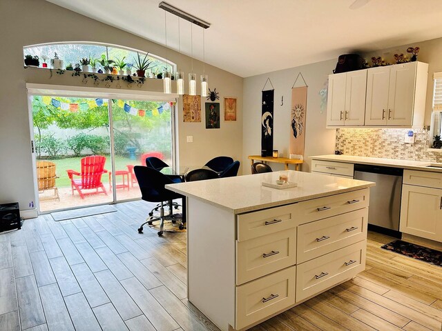 kitchen with pendant lighting, light hardwood / wood-style flooring, decorative backsplash, stainless steel dishwasher, and white cabinetry