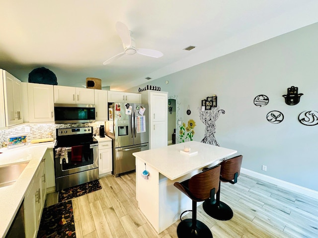 kitchen with white cabinetry, stainless steel appliances, a breakfast bar area, light hardwood / wood-style floors, and decorative backsplash