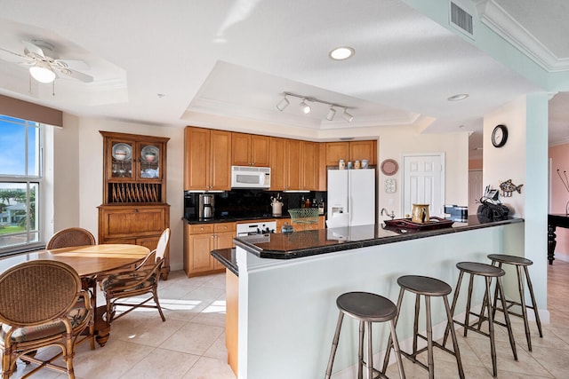 kitchen with decorative backsplash, white appliances, kitchen peninsula, and a tray ceiling