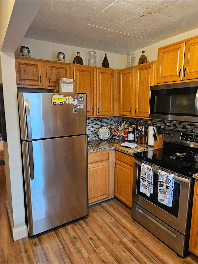 kitchen featuring decorative backsplash, light wood-type flooring, dark stone countertops, and appliances with stainless steel finishes