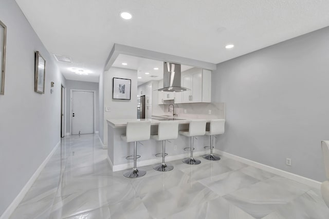 kitchen with kitchen peninsula, a kitchen breakfast bar, sink, wall chimney range hood, and white cabinets