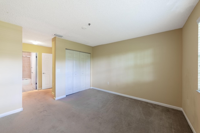 unfurnished bedroom with a textured ceiling, a closet, ensuite bath, and carpet flooring