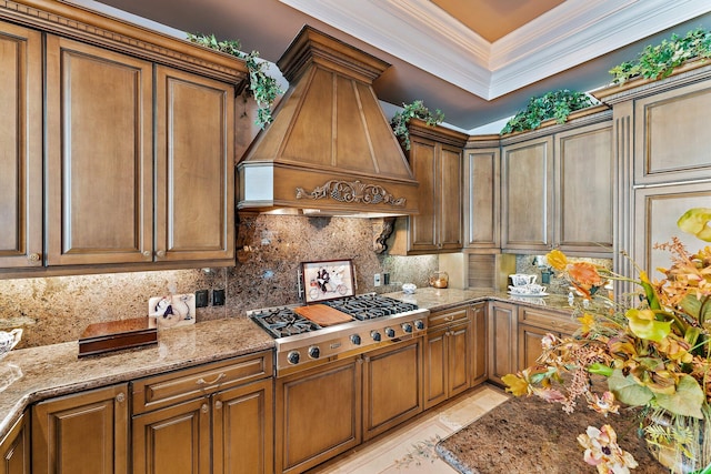 kitchen featuring light stone countertops, premium range hood, tasteful backsplash, ornamental molding, and stainless steel gas cooktop