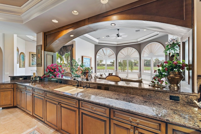 interior space featuring a raised ceiling, ceiling fan, dark stone countertops, and sink