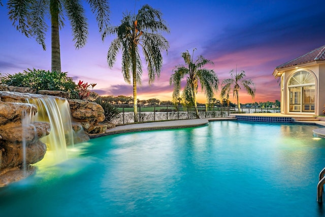 pool at dusk featuring pool water feature