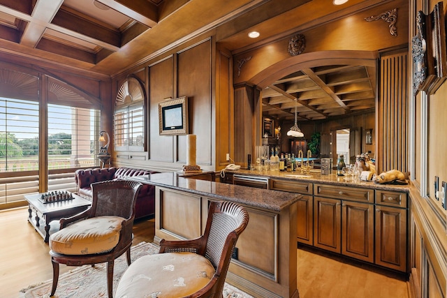 bar with coffered ceiling, decorative light fixtures, stone counters, beamed ceiling, and wood walls