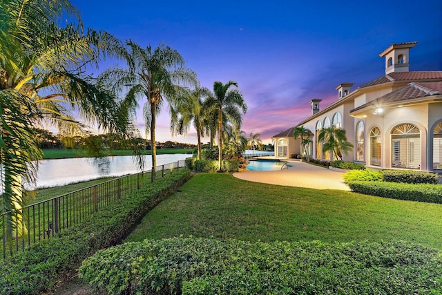 yard at dusk with a water view and a fenced in pool