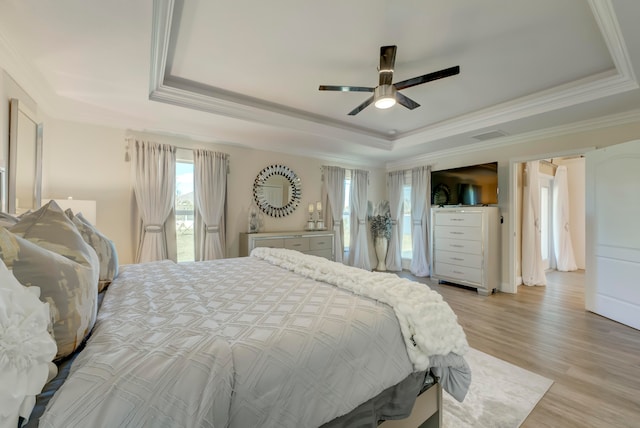 bedroom with ceiling fan, a raised ceiling, light wood-type flooring, and ornamental molding