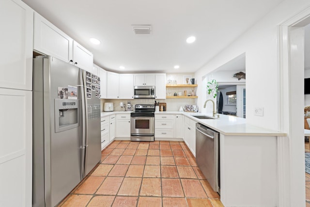 kitchen with kitchen peninsula, decorative backsplash, stainless steel appliances, sink, and white cabinetry