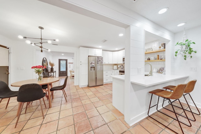 kitchen featuring kitchen peninsula, built in features, appliances with stainless steel finishes, decorative light fixtures, and white cabinetry