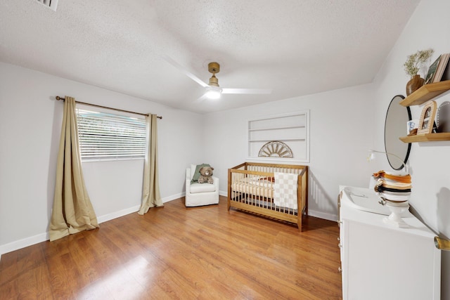 bedroom featuring a crib, light wood-type flooring, a textured ceiling, and ceiling fan